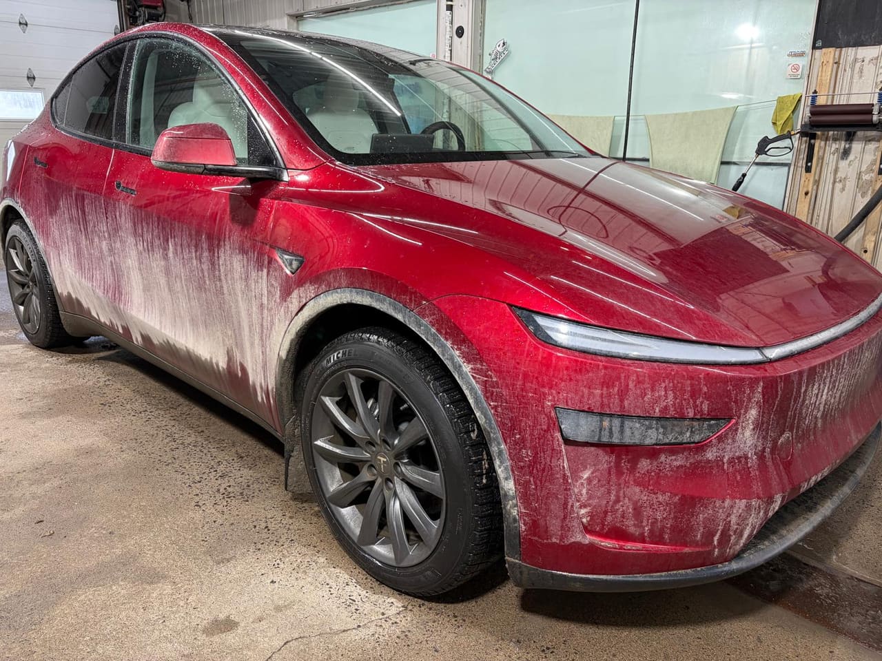 Tesla Model Y rouge couverte de boue séchée sur les portières, les ailes et le pare-chocs